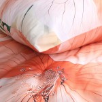 Pościel satyna bawełniana 220x200 Camellia w kolorze kremowym z pomarańczowymi kwiatami. Zbliżenie na poduszkę oraz kołdrę, z wyraźnym wzorem kwiatowym i delikatną fakturą materiału. Wzór ożywia aranżację sypialni.