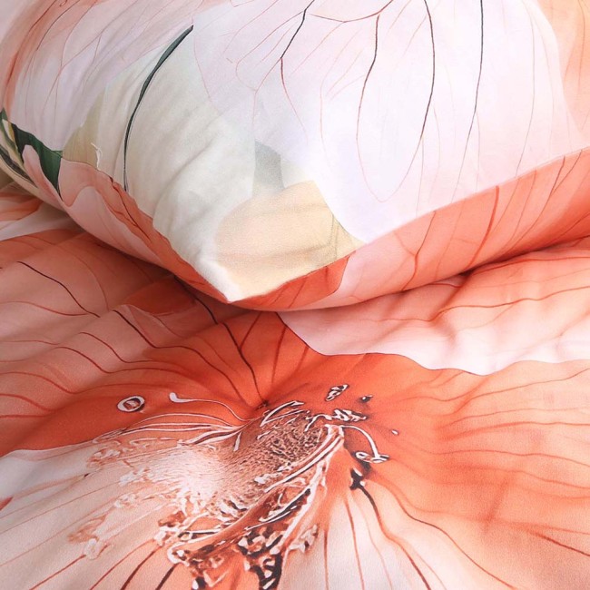 Pościel satyna bawełniana 220x200 Camellia w kolorze kremowym z pomarańczowymi kwiatami. Zbliżenie na poduszkę oraz kołdrę, z wyraźnym wzorem kwiatowym i delikatną fakturą materiału. Wzór ożywia aranżację sypialni.