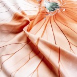 Pościel satynowa w kolorze kremowym z pomarańczowymi kwiatami, wykonana z bawełny. Zbliżenie na delikatną fakturę materiału, z wyraźnie widocznym wzorem kwiatowym oraz subtelnymi liniami.