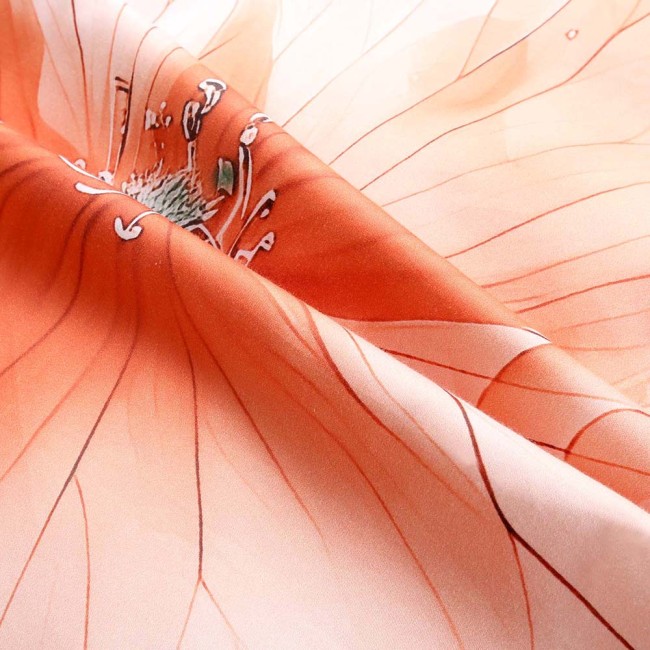 Pościel satyna bawełniana 220x200 w kolorze kremowym z pomarańczowymi kwiatami. Zbliżenie na fakturę materiału, ukazujące delikatne linie i detale wzoru. Produkt leży na płasko, podkreślając jego gładkość i subtelną kolorystykę.