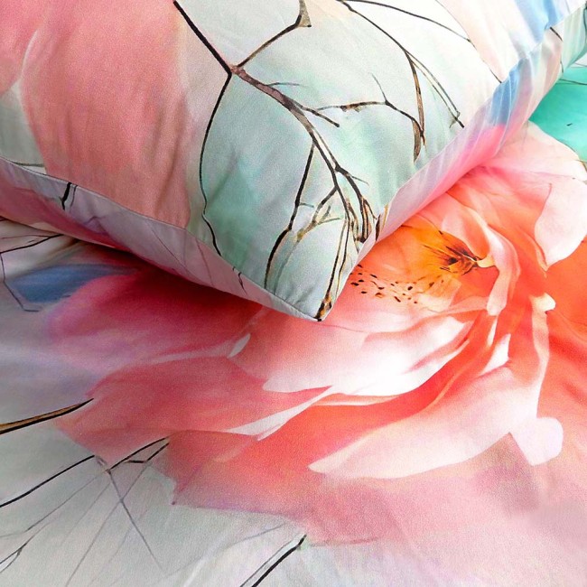 Pościel satynowa w rozmiarze 220x200 cm z szaro-zielonym tłem, zdobiona dużymi różowymi kwiatami i delikatnymi gałązkami. Poduszka leży na narzucie, ukazując gładką teksturę materiału. Wzór ma subtelny, kwiatowy motyw.