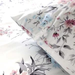 Pościel satynowa 200x220 cm w kolorze białym z wiosennym wzorem różowych i niebieskich kwiatów. Widoczne poduszki i poszwa, materiał gładki, z delikatnym połyskiem. Ułożona na płaskiej powierzchni, prezentująca szczegóły nadruku.