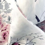 Pościel satyna bawełniana 200x220 w białym kolorze, ozdobiona wiosennymi różowymi i niebieskimi kwiatami. Ujęcie z bliska, ukazujące fakturę materiału oraz detale nadruku na tkaninie.
