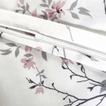 Pościel satynowa bawełniana 200x220 w białym kolorze, zdobiona wiosennymi różowymi i niebieskimi kwiatami. Widoczne zamknięcie na zamek błyskawiczny. Motyw kwiatowy na tle z gałązkami.