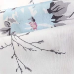 Pościel satyna bawełniana 200x220 cm w kolorze białym, zdobiona wiosennymi różowymi i niebieskimi kwiatami. Wzór przedstawia delikatne gałęzie w odcieniach szarości, tworząc harmonijną kompozycję. Ułożona w złożeniu, ukazująca detale tkaniny.