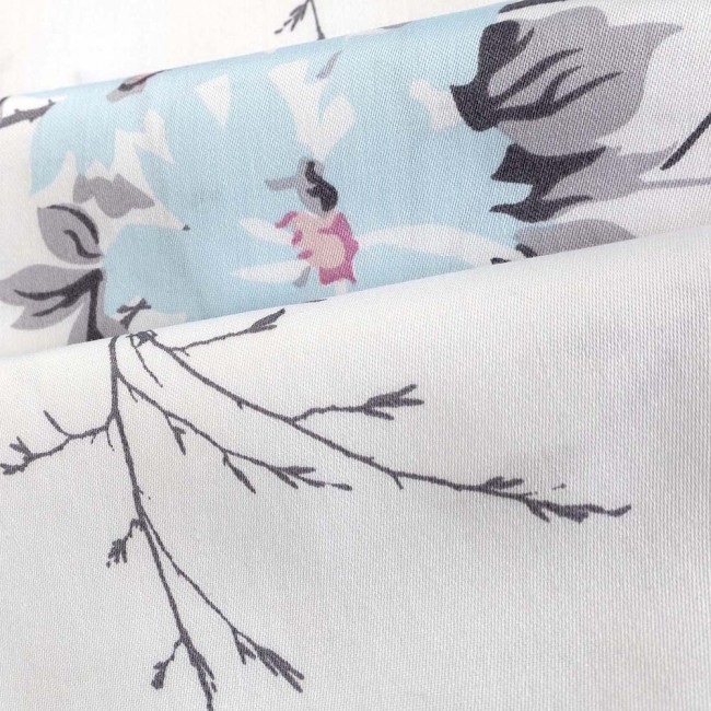 Pościel satyna bawełniana 200x220 cm w kolorze białym, zdobiona wiosennymi różowymi i niebieskimi kwiatami. Wzór przedstawia delikatne gałęzie w odcieniach szarości, tworząc harmonijną kompozycję. Ułożona w złożeniu, ukazująca detale tkaniny.