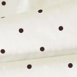 Pościel satyna bawełniana 160x200 w kolorze jasnym z brązowymi kropkami. Złożona, ukazująca teksturę materiału. Proste tło, podkreślające wzór. Idealna do stylizacji sypialni.