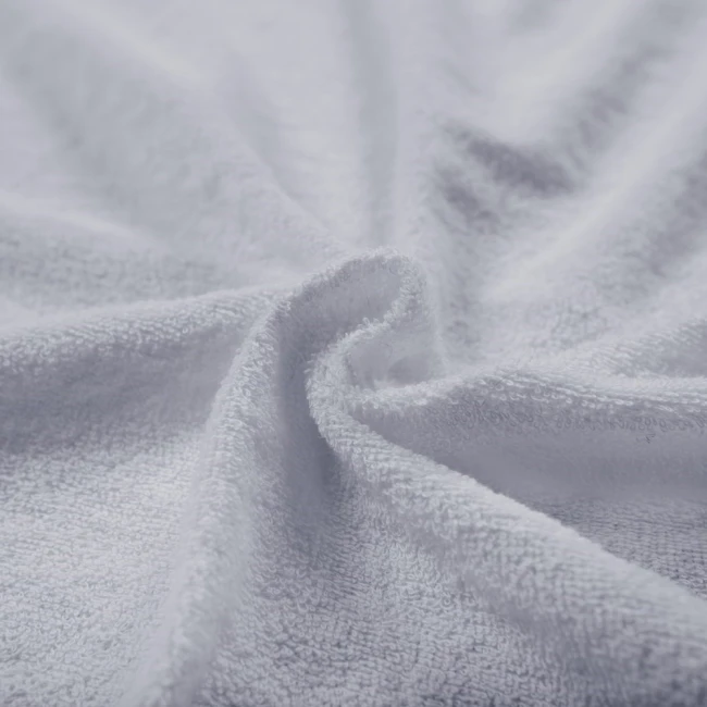 Pościel frotte w kolorze jasno szarym, o wymiarach 135x200 cm. Widoczna tekstura materiału z pętelkami, układająca się w falistą formę. Produkt leży na gładkiej powierzchni, w zbliżeniu na detale materiału.