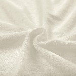 Pościel frotte w kolorze ecru, rozmiar 200x220 cm oraz dwa poszewki 80x80 cm. Materiał o miękkiej, teksturowanej fakturze, układający się w falujące wzory. Ujęcie w zbliżeniu, pokazujące detale tkaniny.