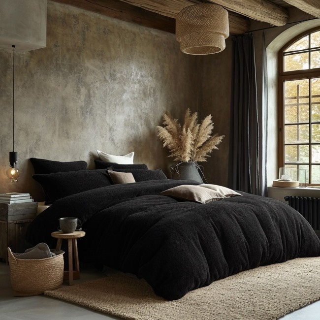 Poszewka frotte 80x80 w kolorze czarnym, z widoczną teksturą materiału, leżąca na poduszce w aranżacji sypialni. W tle naturalne dekoracje oraz stonowane kolory ścian. Produkt w pozycji leżącej, otoczony innymi poduszkami.