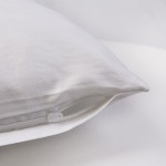 Poszewka satynowa 80x80 w kolorze białym, leżąca na jednolitym tle. Wykonana z gładkiego materiału z zamkiem błyskawicznym, co pozwala na łatwe zakładanie i zdejmowanie. Szczegół widać w dolnym rogu poszewki.