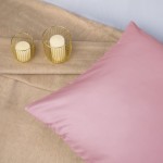 Poszewka satynowa 80x80 w kolorze wrzosowym, leżąca na jasnym, miękkim tle. Widoczne dwa świeczniki z przezroczystymi świecami. Zbliżenie na gładką fakturę poszewki, bez widocznych napisów lub zdobień.