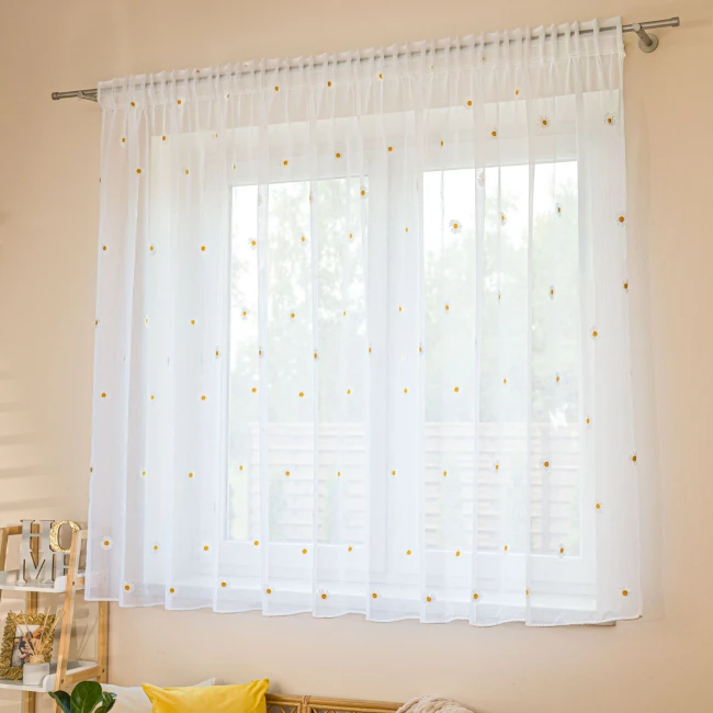 Firana BELLIS o wymiarach 300 x 160 cm, wykonana z etaminy, haftowana w stokrotki, mocowana na taśmie. Biała, z ołowianką, wisząca na karniszu, delikatnie przepuszczająca światło. Tło jasne, minimalistyczne, z elementami dekoracyjnymi w aranżacji.