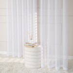 Firana ETAMINA w kolorze białym, o wymiarach 200x250 cm, zawieszona na srebrnych przelotkach. Widoczna w aranżacji z jasnym tłem, obok białego stołka z książkami i dekoracyjnym wazonem z patyczkami. Tkanina lekka i przezroczysta.