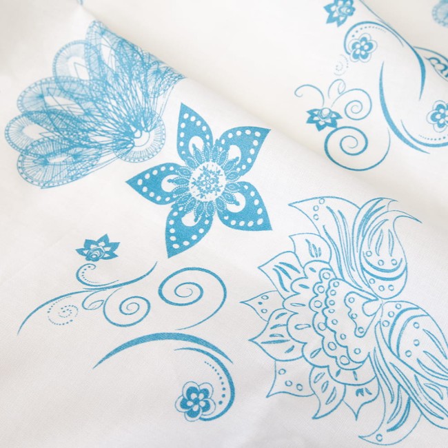 Pościel bawełniana 220x200 Cottonlove w kolorze białym z niebieskim wzorem kwiatów i organicznych kształtów, leżąca na płaskiej powierzchni. Widoczne detale wzorów i faktura materiału, podkreślająca jego miękkość.