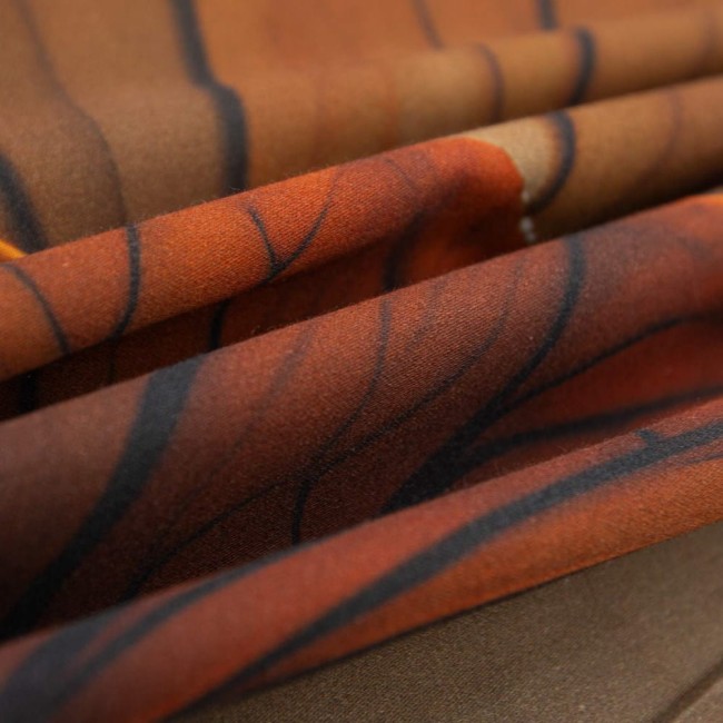 Beżowa pościel satynowa 220x200 Satynlove Premium z liściastym wzorem. Ułożona w fałdy, ukazująca gładką, połyskującą teksturę. Zbliżenie na detale wzoru z ciemnymi akcentami w kształcie gałęzi.