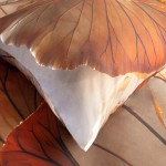 Pościel satyna bawełniana 220x240 Satynlove Premium w kolorze beżowym z wzorem liści. Ułożona na łóżku w złożonym stanie, z poduszką w zbliżeniu. Wyraźne detale wzoru i faktury materiału, matowe i błyszczące wykończenie. Tło w naturalnych odcieniach.