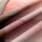 Pościel satyna bawełniana 220x200 w odcieniach różu i szarości, z nadrukiem kwiatów. Złożona, ukazująca gładką fakturę tkaniny. W tle jasne, neutralne, co eksponuje wzory i kolory materiału.