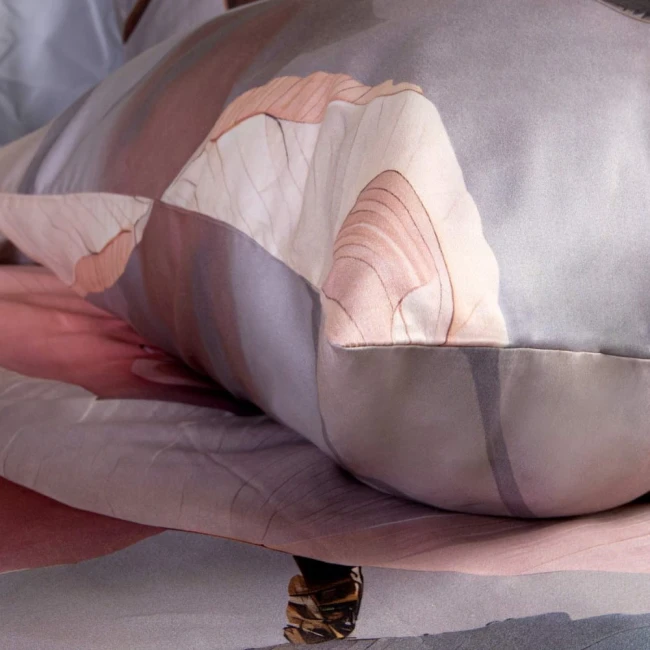 Pościel satyna bawełniana 220x200 cm w kolorze różowym i szarym, z delikatnym wzorem kwiatowym. Zbliżenie na poduszkę, eksponującą gładką fakturę materiału i subtelne przejścia kolorystyczne. Rozłożona na łóżku, na jednolitym tle.