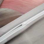 Zbliżenie na różową i szaro-beżową pościel satynową z kwiatowym wzorem. Widoczny zamek błyskawiczny z białą taśmą. Materiał gładki, satynowy, z lekkim połyskiem, prezentujący subtelne odcienie kolorów.