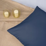 Poszewka satynowa 70x80 w kolorze chabrowym leży na jasnym, miękkim tle. Produkt ma gładką, błyszczącą powierzchnię i kształt kwadratu. Obok znajdują się dwa szklane świeczniki w złotej osłonie z białymi świecami.