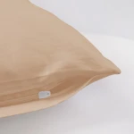 Poszewka satynowa 70x80 w kolorze jasnego beżu, leżąca na jasnym tle. Widoczny zamek błyskawiczny w białym kolorze. Gładka, błyszcząca faktura, bez wzorów czy napisów. Ujęcie z boku, ujawniające miękkie linie i kształt poszewki.