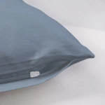 Poszewka satynowa 70x80 w kolorze błękitnym, z zamkiem błyskawicznym, leżąca na jasnym tle. Widoczna gładka faktura materiału, bez wzorów czy napisów. Ujęcie z boku podkreśla elegancki wygląd oraz detale wykończenia.