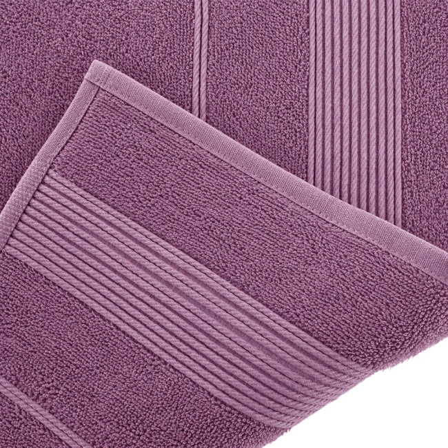 Bambusowy ręcznik o wymiarach 50x90 cm w kolorze lawendy, leżący na boku. Widoczna miękka faktura materiału oraz delikatne zdobienie w postaci poziomych pasków. Brzeg ręcznika wykończony subtelną lamówką.
