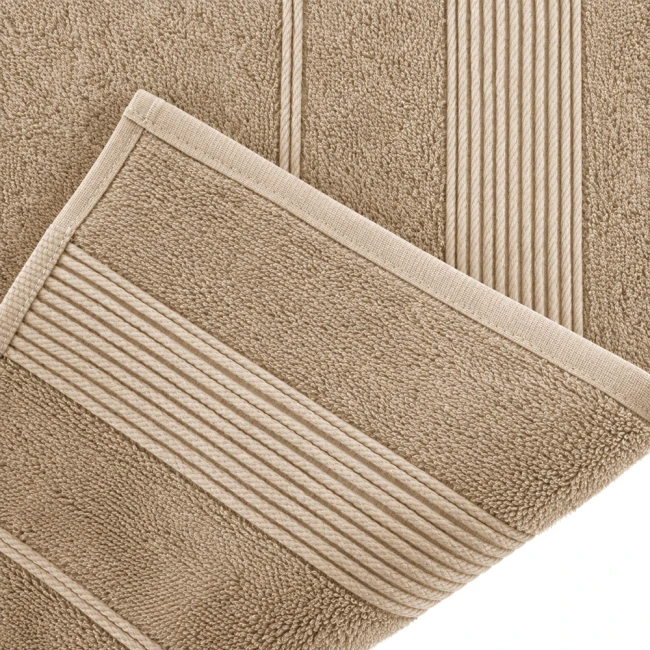 Ręcznik bambusowy 70x140 w kolorze cappuccino, leżący na jasnym tle. Widoczne napisy w formie drobnych, poziomych pasów na jednym z brzegów. Materiał o miękkiej, teksturowanej fakturze. Złożony brzegi z delikatnym obszyciem.