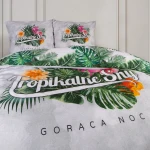 Pościel bawełniana 160x200, wzór tropikalny, z nadrukiem zielonych liści i kolorowych kwiatów na jasnoszarym tle. Zestaw zawiera poszewki na poduszki z napisem Tropikalne Sny. Produkt leżący na łóżku, z bliska prezentujący detale wzoru oraz tekst.