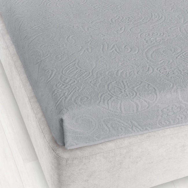 Prześcieradło żakardowe bez gumki w kolorze popielatym, o wymiarach 175x220 cm, leżące na łóżku. Detal przedstawia delikatny wzór, teksturę i fakturę materiału. Tło jasne, prostokątne, prezentujące estetykę aranżacji sypialnianej.