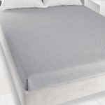 Prześcieradło żakardowe bez gumki w kolorze popielatym, o wymiarach 175x220 cm, rozłożone na łóżku. Posiada delikatny wzór w fakturze. W tle widoczna jest część jasnego materaca i białe poduszki.