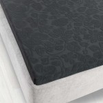 Prześcieradło żakardowe bez gumki 150x205 w kolorze grafitowym. Widok z góry, na rozłożonym materacu. Wzór kwiatowy o delikatnej fakturze, matowy materiał, dobrze dopasowane do krawędzi. Tło w jasnym odcieniu dla lepszej widoczności produktu.